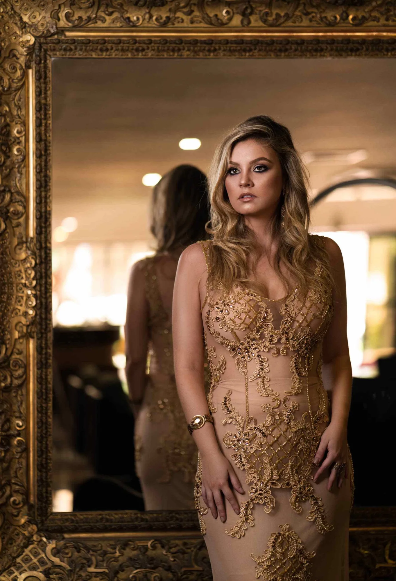 A woman wearing a gold embroidered dress beside a mirror