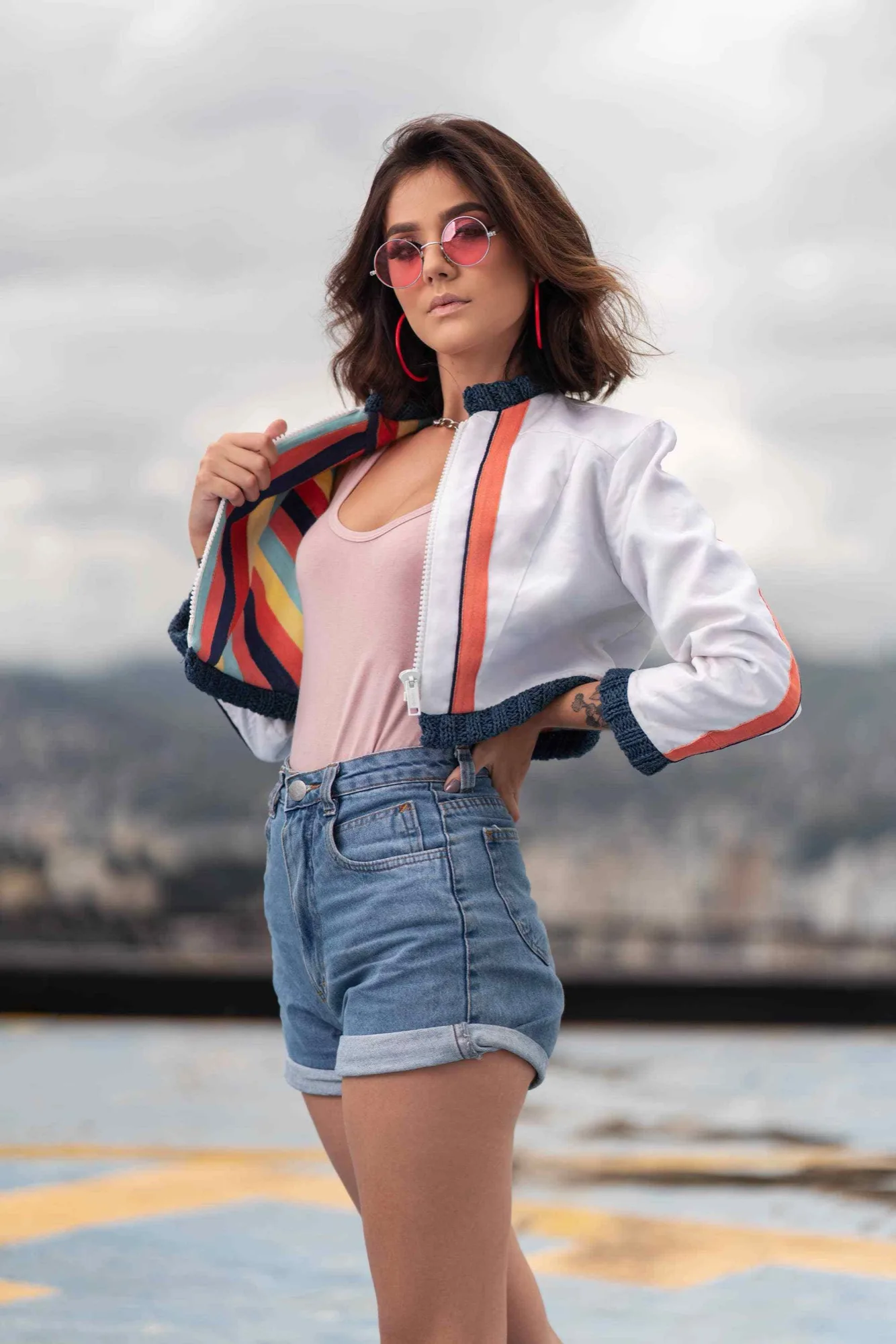 A woman with pink sunglasses and a white jacket in an urban session